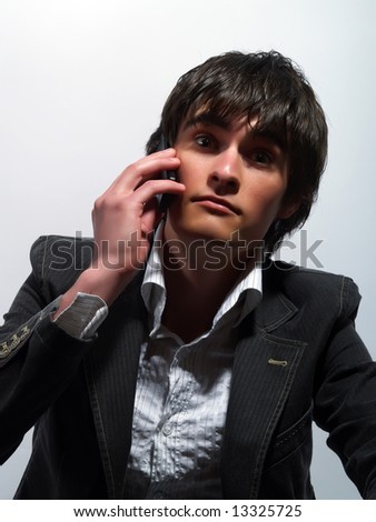 A portrait about a trendy handsome guy who is calling somebody and he is surprised. He is wearing a white shirt and a stylish black suit.