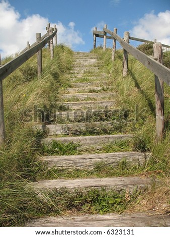 Stairs on a grassy dune lead up to a blue sky with clouds like a stairway to heaven.