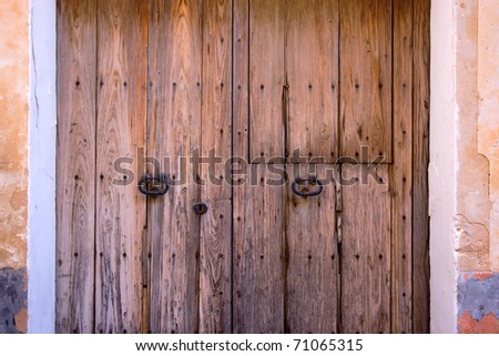 Fragment of old wooden door with oxidized forged steel knockers and screws in simple stone wall of facade.  Texture of wood.