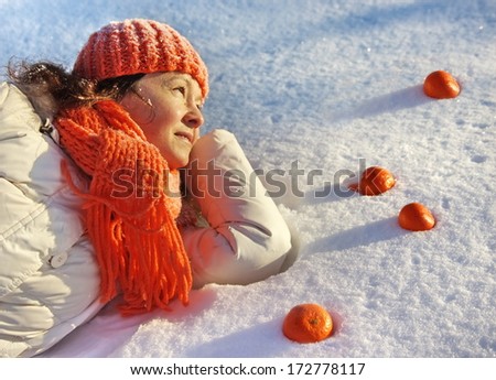 A woman lying on the snow with tangerines around her