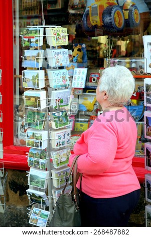 BAKEWELL, DERBYSHIRE, UK. APRIL 08, 2015.  A senior lady browsing through postcards outside a shop at Bakewell in Derbyshire, UK.