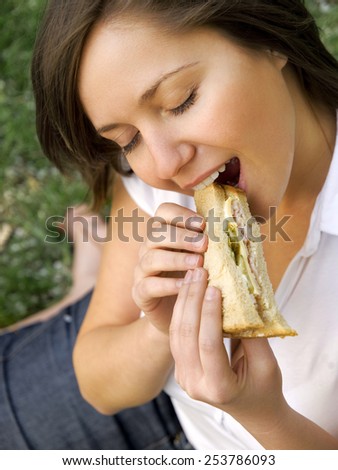 Young woman eating sandwich outdoors, close up