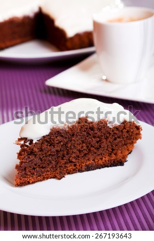 Chocolate cake with white cream, with one piece cut from the whole cake in a plate, coffee cup in the background