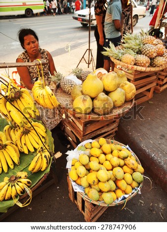 Yangon, Myanmar - February 24, 2011 : Senior Burmese woman selling fresh fruits in the street market - mango, pineapple and bananas