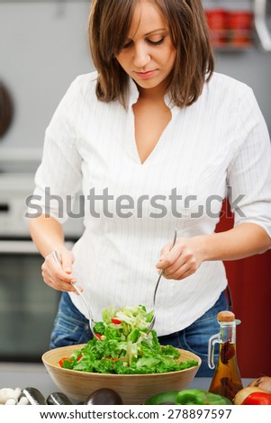 Young woman making salad in the kitchen and pooring olive oil