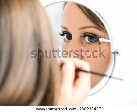 Applying make-up on young woman face, reflection in the mirror