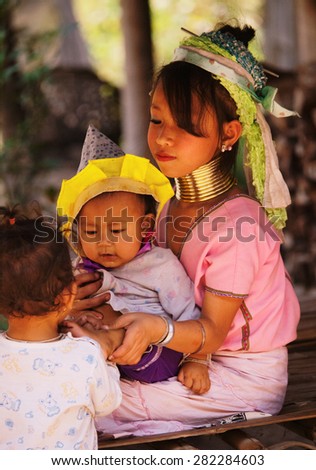 Chian Mai, Thailand - March 07, 2011 : Street portrait of a young long-neck woman holding a baby and young boy. There are 25 copper rings on her neck weighting 9 kilograms.