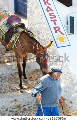 Fira, Greece - May 04, 2012 : Local Greek man with a donkey - tourists enjoy riding a donkey instead of climbing the 600 steps to the top of the village