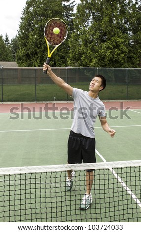 Young Asian Man taking an overhead volley on outdoor tennis court