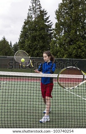 Young girl taking volley against opponent at the net with green trees in background
