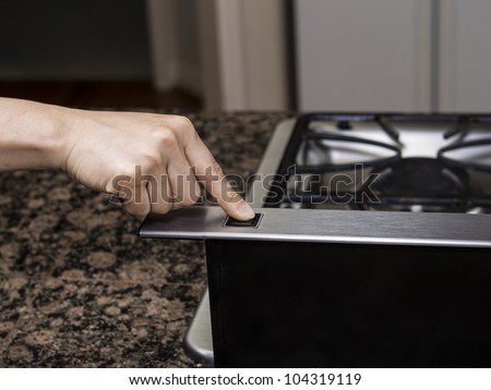 Index finger pushing fan button on top of gas stove range