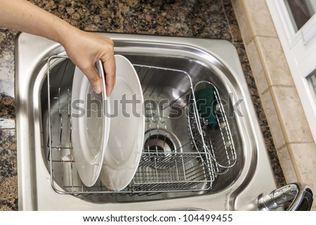 Hand placing white dishes into drying pan in kitchen sink