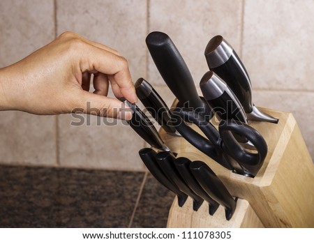 Hand selecting knife out of full set on kitchen counter top