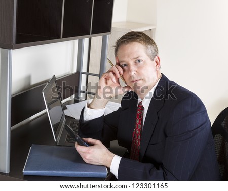 Mature man holding calculator while thinking with computer and papers on desk