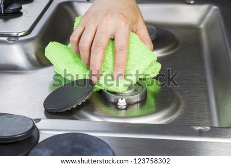 Hand wiping clean stove top and burner covers with green microfiber cloth