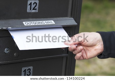 Horizontal photo of male hand putting letters into outgoing postal mailbox with green grass in background