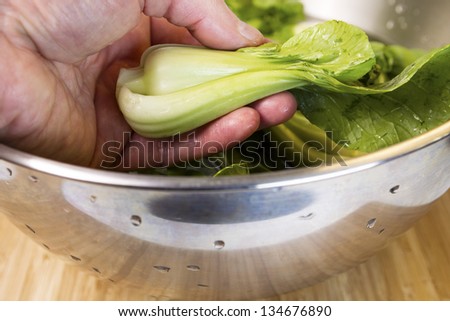Closeup horizontal photo of male hand washing Chinese Choy vegetable in Stainless Steel bowl on natural bamboo wood