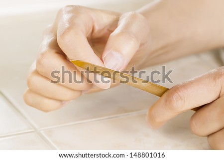 Close up horizontal photo of female hands with golden metal nail file tool in front