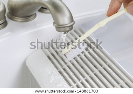 Close up horizontal photo of female hand with tooth brush cleaning bathroom fan vent cover in bathroom sink