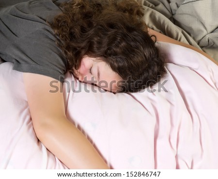 Young girl too tired to wake up in the morning while lying face down in bed