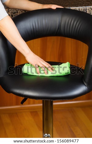 Vertical photo of female hand cleaning kitchen leather chair with green microfiber rag with red oak floor and Center Island in background