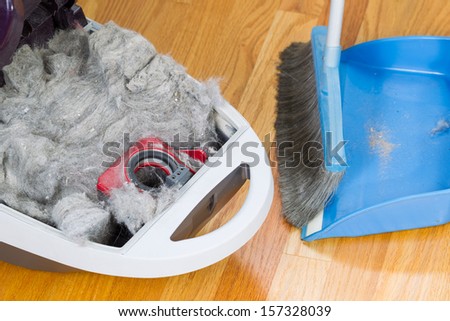 Horizontal photo completely filled dirty vacuum cleaner with hardwood floors, dust pan and broom in background