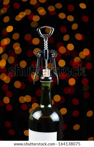 Vertical photo of Red Wine bottle and metal hand opener on top of cork with holiday lights in the background