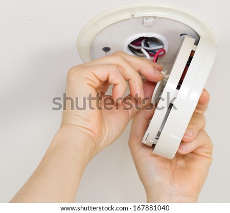 Horizontal photo of female hands taking home smoke detector apart with white ceiling background