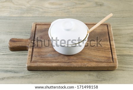Horizontal photo of white porcelain cooking pot on black walnut serving board with aged wood underneath