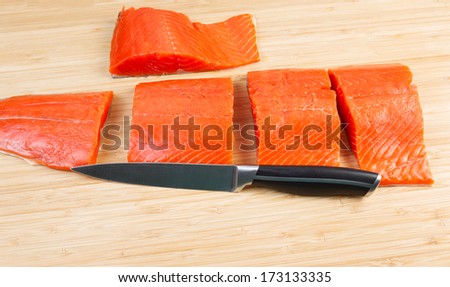 Horizontal photo of fresh Wild Red Salmon pieces from Fillet with cutting knife in front and bamboo board underneath