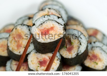 Closeup horizontal photo of a single spicy tuna roll on top of sushi stack being picked up with chopsticks