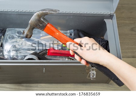 Horizontal photo of female hand taking old hammer out of toolbox with aged wooden floors in background