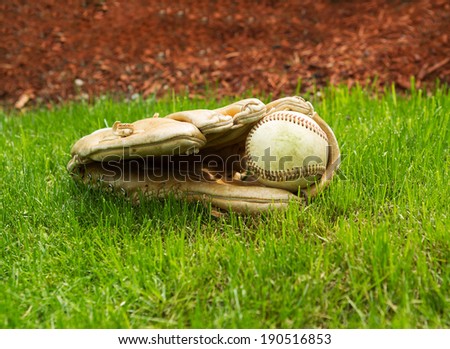 Closeup horizontal photo of old baseball inside of used glove on natural grass field