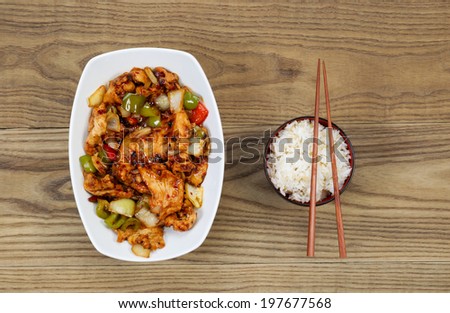 Overhead view of Chinese spicy chicken dish and rice in bowl with chopsticks placed on rustic wooden boards.