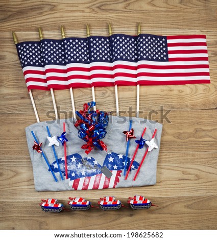 Overhead view of United States of America flags, ribbons, t-shirt, fire cracker, dog tag and pinwheels positioned on rustic wooden boards.