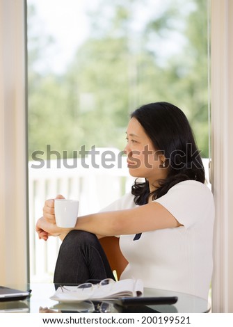 Vertical image of mature woman relaxing while working from home with bright daylight coming in from window in background