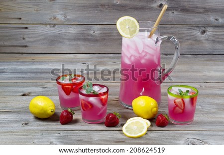 Front view of freshly made pink lemonade with whole lemons, strawberries and filled glasses on rustic wood