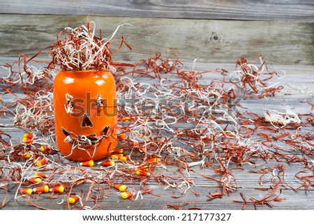 Horizontal image of a scary orange pumpkin jar filled with shredded paper placed on rustic wooden boards