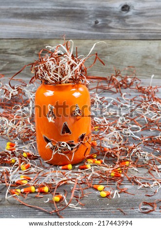 Vertical image of a scary orange pumpkin jar filled with shredded paper placed on rustic wooden boards