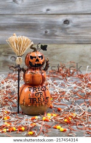 Vertical image of a scary orange pumpkin figure holding straw broom placed on rustic wooden boards