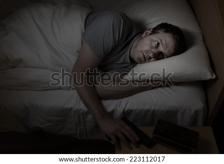 Mature man reaching for pistol in dark bedroom with scared look on his face