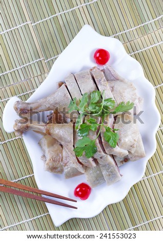Vertical top view image of Chinese cooked chicken, parsley, cherry and chopsticks in shell shaped white plate with natural bamboo place mat background