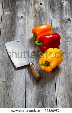 Vertical image of three fresh bell peppers and old butcher knife on aged wooded boards