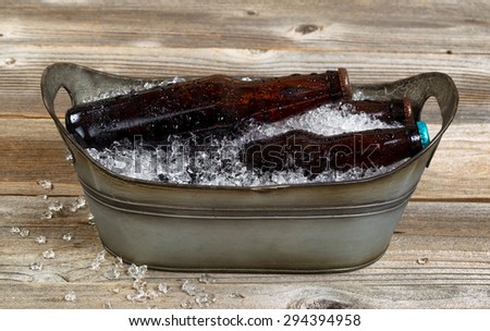 Vintage metal tub shaped bucket filled with crushed ice and bottled beer on rustic wooden boards.
