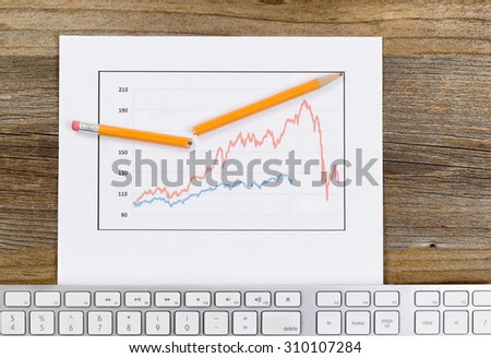 High angled view of line graph, broken pencil and computer keyboard on rustic desktop.