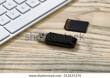 Close up of data thumb drive and memory flash card. Computer keyboard in background on desktop.