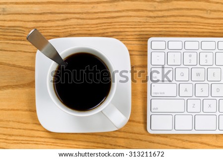 Top view of desktop with coffee, selective focus on top of cup, and partial keyboard. Horizontal format.