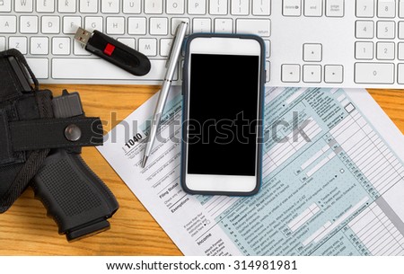 Top view of service weapon, keyboard, pen, thumb drive and IRS tax form on desktop. Audit concept.