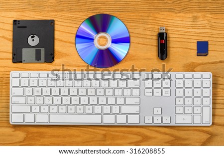 Top view of desktop with keyboard, diskette, CD, thumb drive, and Flash disk. Concept of portable data storage device with technology changes.