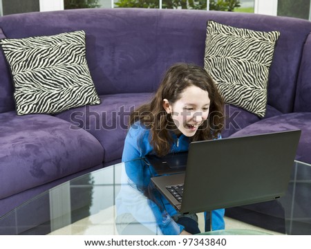 Young girl looking at laptop while laughing with couch in background